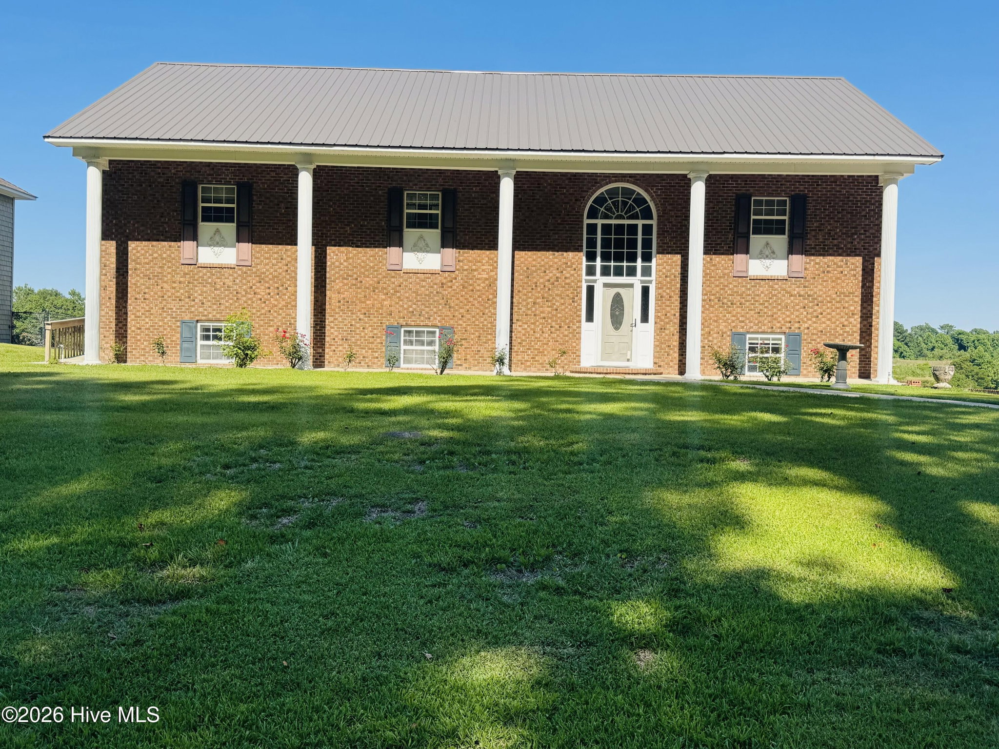 Daytime front elevation of 888 Sea Gate Drive, a symmetrical two-story brick home with four white portico columns, an arched fanlight over the front door, and a wide green lawn