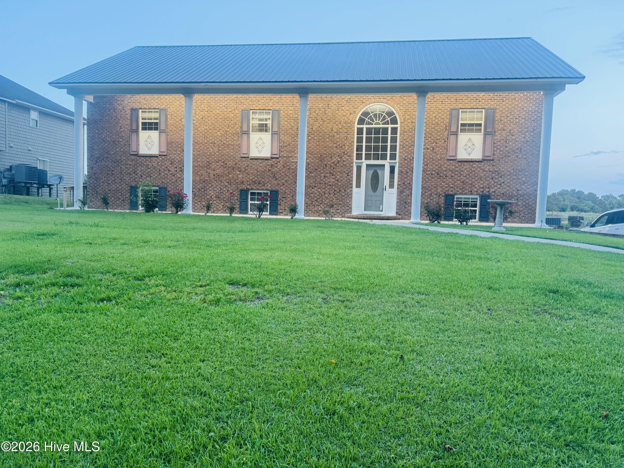 888 Sea Gate Drive photographed at dusk, the brick front and white columns under a soft lavender evening sky with the lawn in the foreground