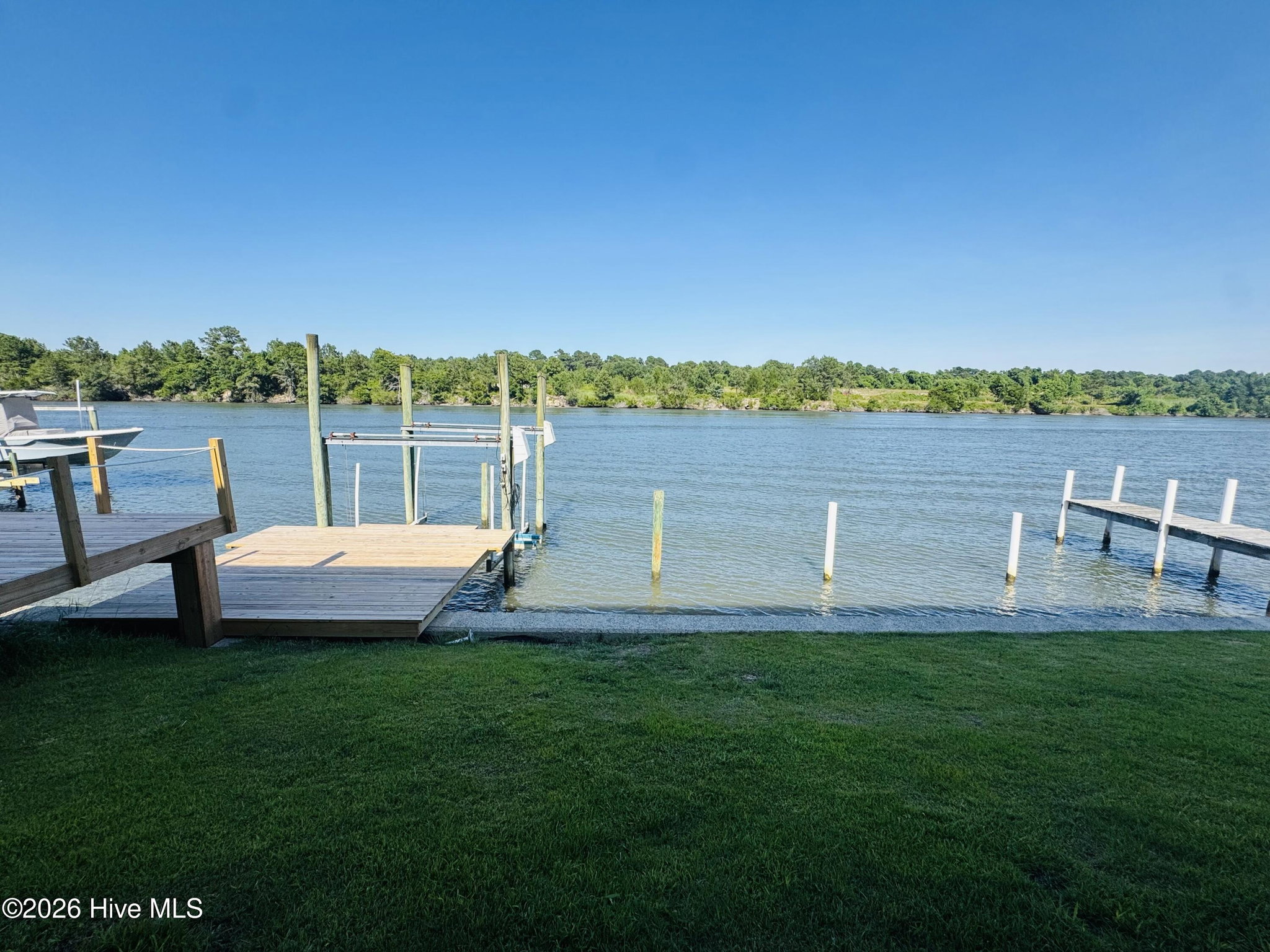 Wide view from the back lawn of 888 Sea Gate Drive across the green grass to the wooden pier and the broad Intracoastal Waterway, with a forested shoreline on the far side