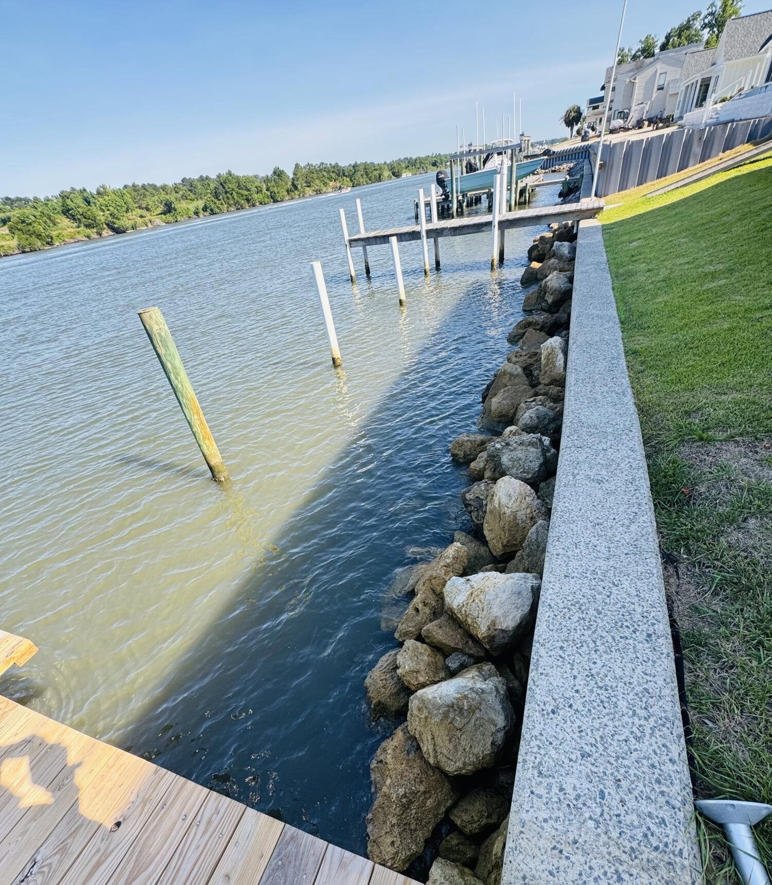 Riprap rock seawall lining the water's edge below 888 Sea Gate Drive, with wooden dock decking in the foreground and dock pilings standing in the calm waterway