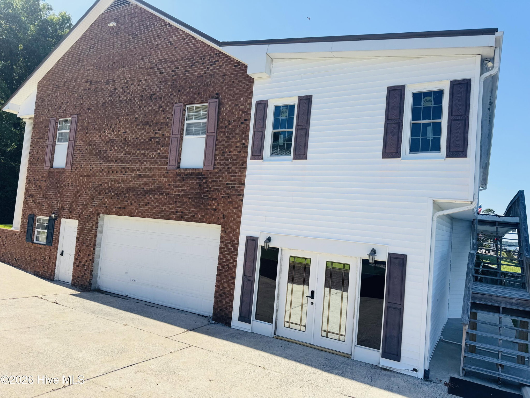 Rear and side of 888 Sea Gate Drive showing brick on the lower level, white siding above, an attached two-car garage, and ground-floor French doors opening toward the water