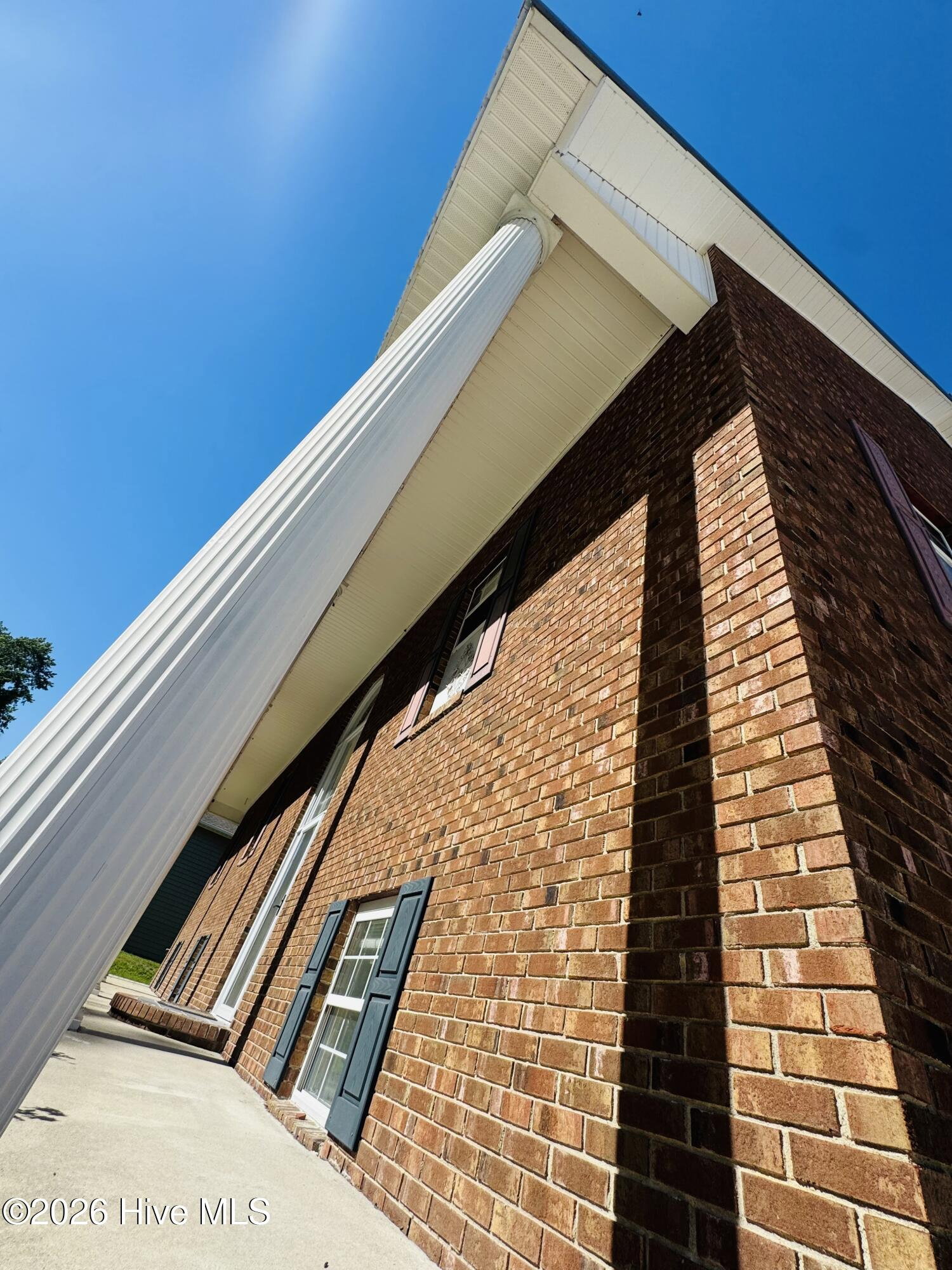 Architectural detail of 888 Sea Gate Drive, a tall white portico column rising along the corner of the brick wall against a clear blue sky